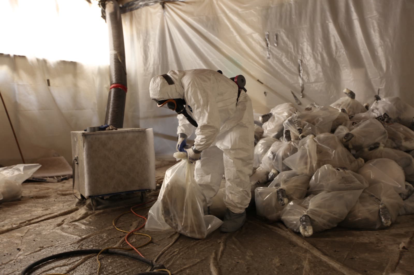 Operari amb EPI complet embossant residus d'amiant en una zona confinada