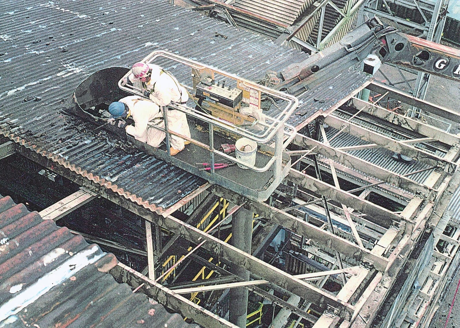 Dos operarios con buzo y mascarilla retirando placas onduladas desde una plataforma
